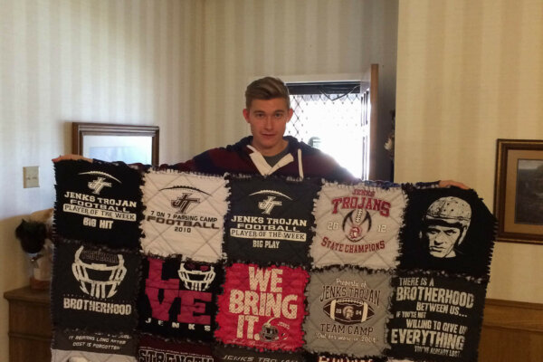 Young man holding a tshirt quilt in maroon and gray colors