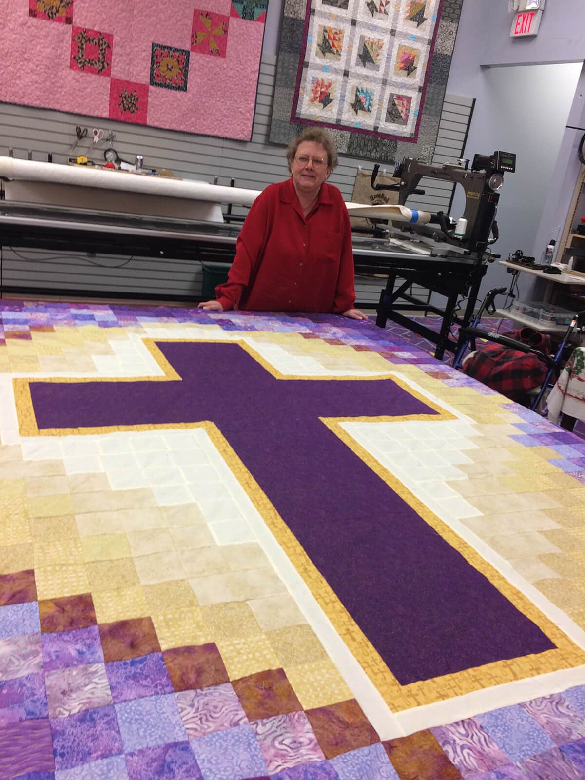 Photo of woman standing behind a quilt top with a cross motif.