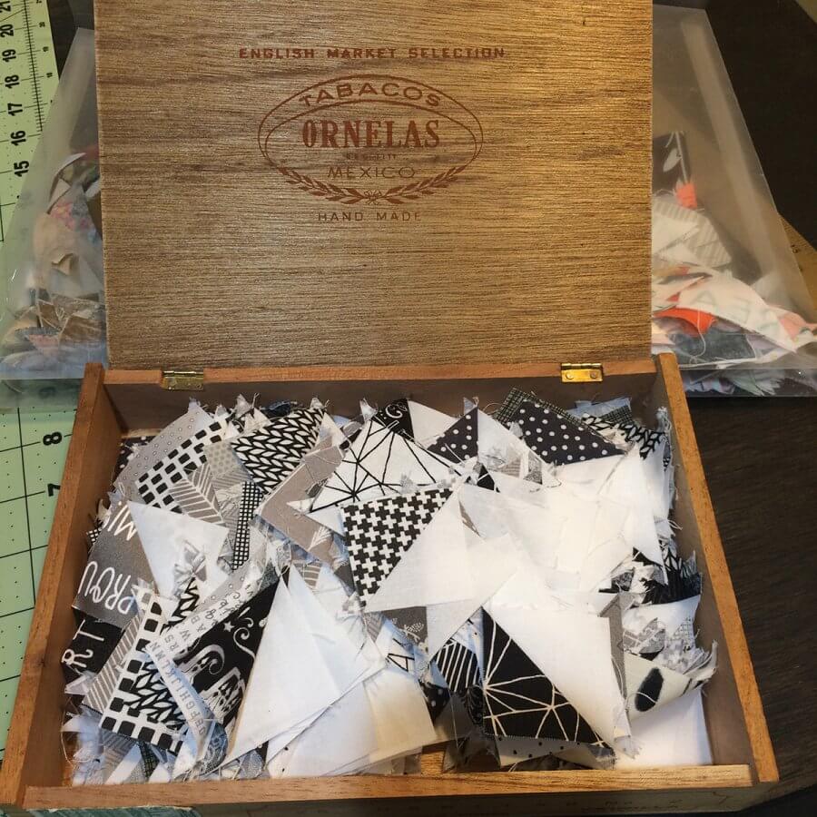 Photo of a cigar box full of black and white Half Square Triangles made from leftover Quick Corners