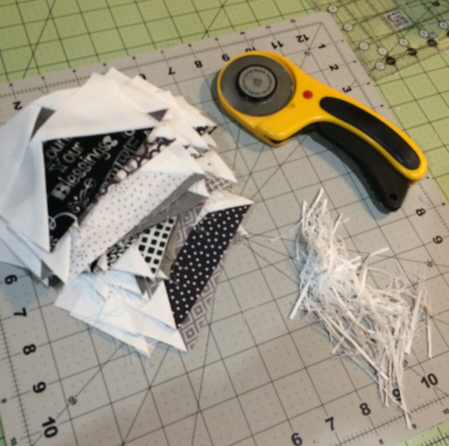 Photo of a stack of trimmed flying geese quilt block units beside a yellow Olfa rotary cutter