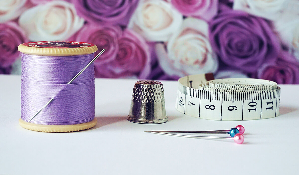 photo of a purple stacked spool of thread with a needle in it, a thimble, pin and measuring tape