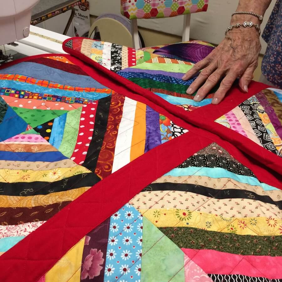 Photo of a scrappy strip quilt that Emma is using to teach "Quilt as you go" techniques.