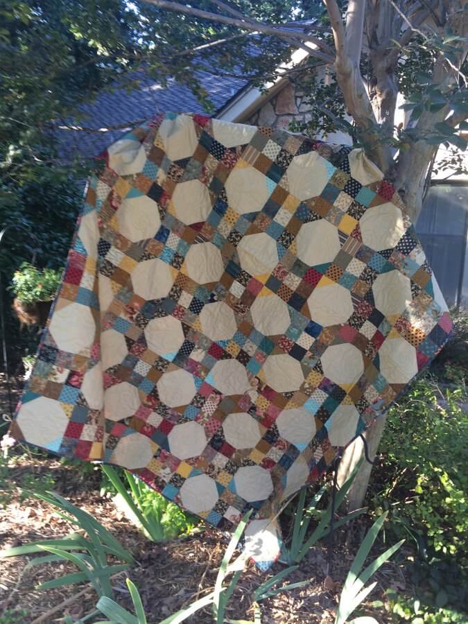 photo of 9-patch snowball quilt hanging on ladder under a tree