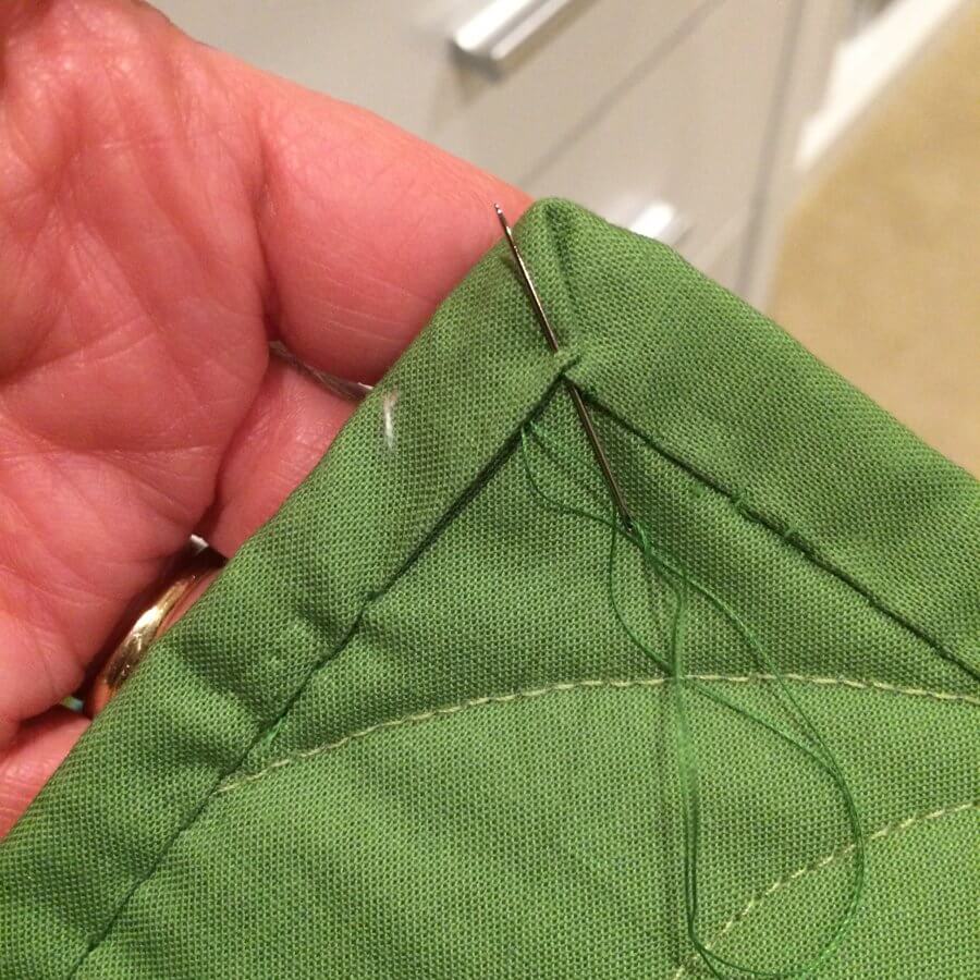 Photo of hand-sewing binding to a quilt with mitering the corner