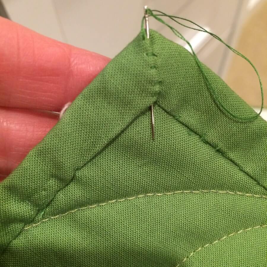 Photo showing needle placement when mitering the corner when hand-sewing the binding to the quilt